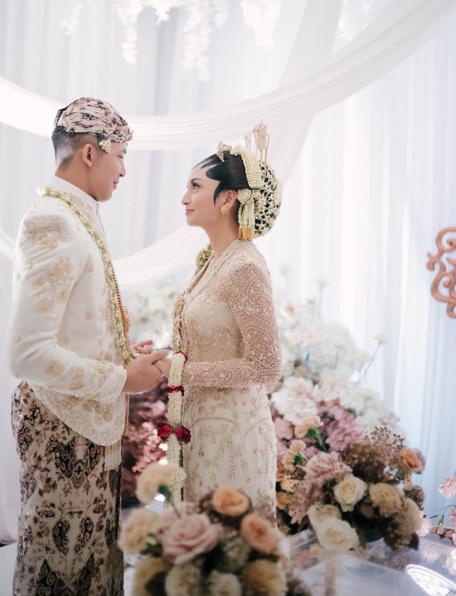 Kedua pengantin tampil kompak dalam balutan busana adat Jawa Solo berwarna putih gading. Diketahui busana pengantin yang dikenakan berasal dari KaaraBride by Mutiara Meddyan. Foto: Instagram/@valtifanka