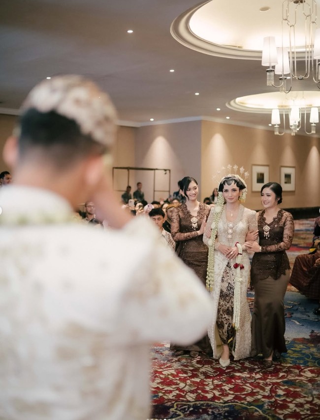 Momen pertama Mochammad Andhika bertemu dengan Valerie di hari pernikahannya. Sambil digandeng oleh kedua bridesmaid yang salah satunya ialah Febby Rastanty, Valerie tampil menawan dengan kebaya lengkap dengan sanggul, paes, dan ronce melati di kepalanya. Foto: Instagram/@valtifanka