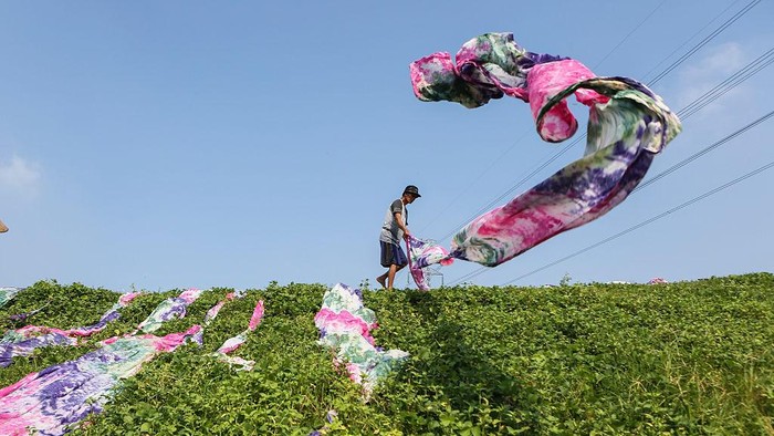 A worker dries traditionally patterned beach fabrics under the scorching sun at a home-based garment industry center in Sukoharjo, Central Java, Indonesia, on May 1, 2025. According to Statistics Indonesia (BPS), as of August 2024, 83.83 million people, equivalent to 57.95% of the total employed population, work in the informal sector. (Photo by Agoes Rudianto/NurPhoto via Getty Images)