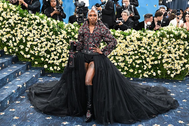 Cynthia Erivo berpose percaya diri di karpet merah Met Gala 2025 dengan no pants look. Dia mengenakan jaket struktural dengan bodis korset yang dihiasi manik-manik merah berbentuk bunga. Pemain film Wicked itu memadukan jaketnya dengan celana pendek hitam (boy shorts) dipadukan dengan rok tulle dramatis model high-low yang memperlihatkan tato di pahanya. Foto: Variety via Getty Images/Gilbert Flores