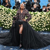 Cynthia Erivo berpose percaya diri di karpet merah Met Gala 2025 dengan no pants look. Dia mengenakan jaket struktural dengan bodis korset yang dihiasi manik-manik merah berbentuk bunga. Pemain film Wicked itu memadukan jaketnya dengan celana pendek hitam (boy shorts) dipadukan dengan rok tulle dramatis model high-low yang memperlihatkan tato di pahanya. Foto: Variety via Getty Images/Gilbert Flores