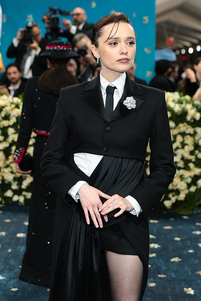 Bintang serial White Lotus, Aimee Lou Wood, debut di Met Gala 2025 dengan gaya pantless. Aimee memakai jaket cropped hitam yang dipadukan dengan kemeja putih dan dasi hitam. Bagian bawah busananya menampilkan desain unik, sebelah sisi berupa rok panjang terbuka dari sutra, sementara sisi lainnya berupa celana super pendek. Foto: Getty Images for The Met Museum//Dimitrios Kambouris