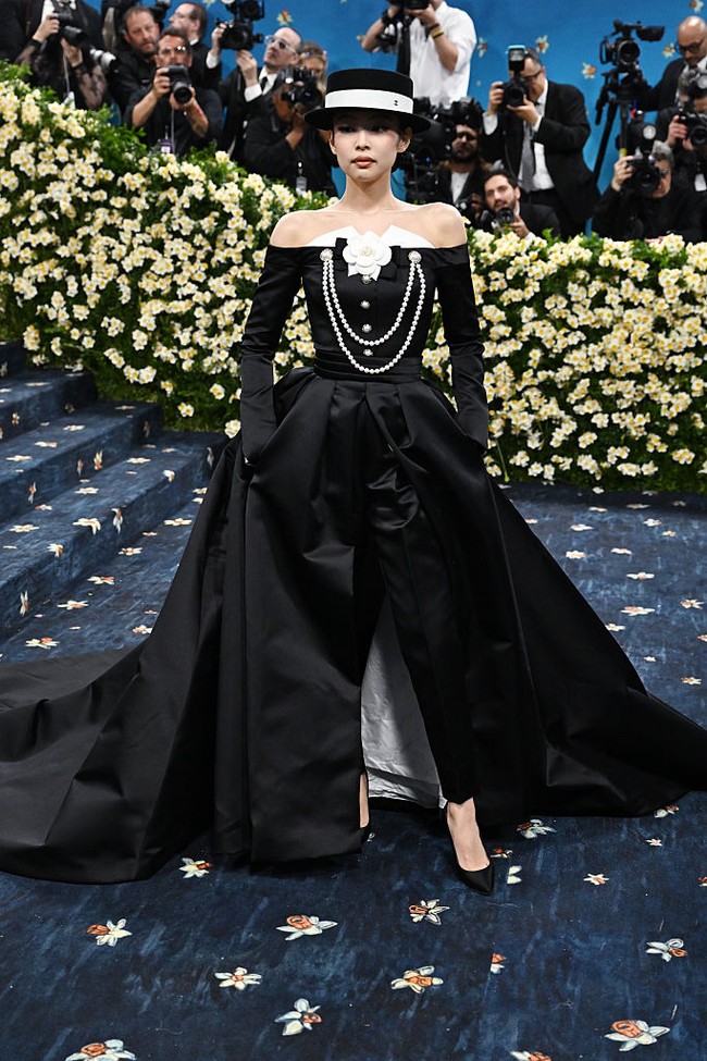 Gaun hitam dengan garis leher off-shoulder apik berpadu bersama celana pensil di bawahnya. Ekor bervolume menyentuh lantai membuat penampilan Jennie kali ini lebih dramatis. Foto: Kevin Mazur/Getty Images for The/Kevin Mazur/MG25