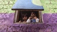 Anak-anak melihat dari balik jendela rumah yang telah dicat warna-warni usai peresmian Lembur Katumbiri oleh Pemerintah Kota Bandung, yang mengusung nilai budaya lokal dan keterlibatan masyarakat.