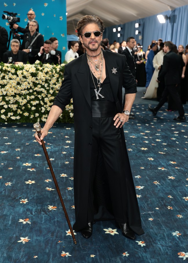 Kehadiran King of Bollywood, Shah Rukh Khan menjadi kejutan di Met Gala 2025. Sang aktor tampil memukau dalam balutan setelan blazer panjang berwarna hitam rancangan desainer populer India, Sabyasachi. Dilengkapi tumpukan kalung emas di atas atasan berkerah rendah dan tongkat kepala harimau sebagai statement. Foto: Getty Images