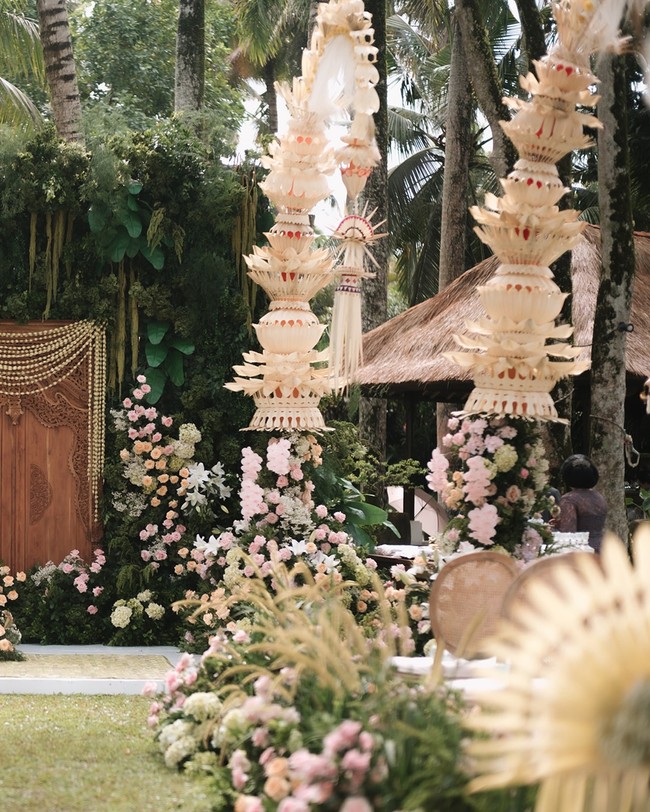 Penjor berhiaskan janur yang menjulang tinggi dan berkelok indah juga menjadi titik fokus. Elemen khas Bali ini menghiasi sisi kanan dan kiri altar, memberikan sentuhan budaya yang kuat sekaligus simbol doa dan persembahan untuk keberkahan. Foto: Instagram/@iluminen