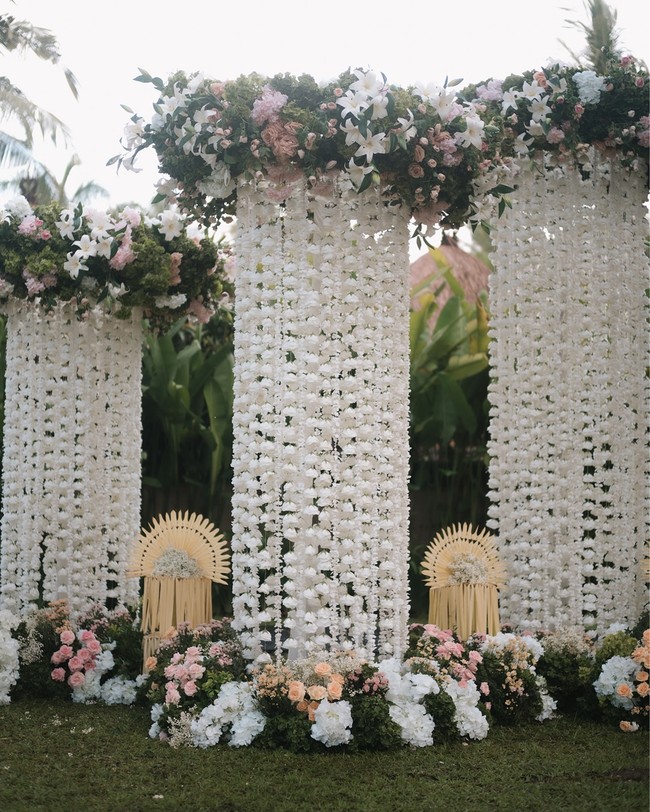 Kombinasi bunga mawar, lily, dan hydrangea disusun cantik di sepanjang jalan masuk, area altar, hingga melingkari penjor. Foto: Instagram/@iluminen