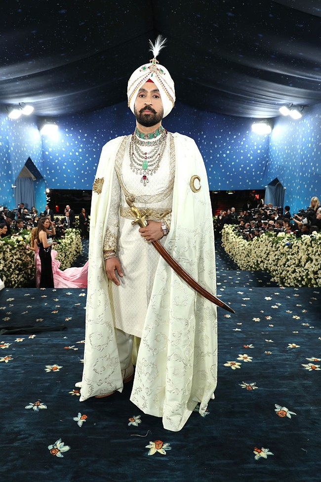 Diljit Dosanjh menampilkan warisan budayanya di Met Gala 2025. Aktor Bollywood itu memakai kostum busana rancangan Prabal Gurung yang terdiri dari sherwani bernuansa ivory, tehmat atau celana panjang kain dililit, hingga sorban berlapis permata. Tampak pula kirpan alias pedang berkepala singa di tangan kanannya. Foto: Getty Images