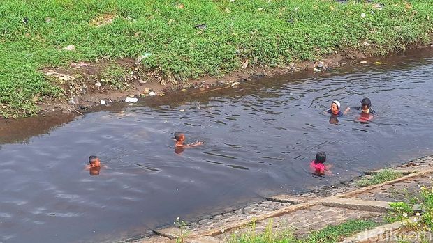 Sejumlah anak-anak tengah berenang di aliran air sungai berwarna hitam