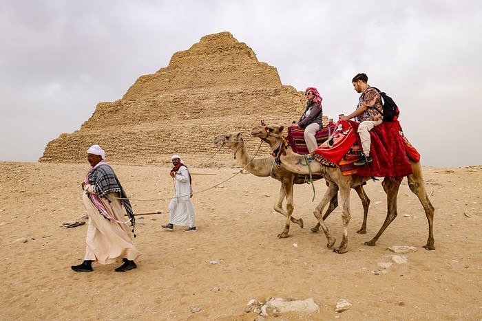 GIZA, EGYPT - MAY 4: Tourists ride on camels as Zoser Pyramid is seen behind at the historical Saqqara region, which is home to the majority of historical artifacts from ancient Egypt, in Giza, Egypt on May 4, 2025. King tombs, temples, small pyramids and the region, where the Zoser Pyramid, which is estimated to have been built in the 2700 B.C. is located, considered an open-air museum. (Photo by Nurettin Boydak/Anadolu via Getty Images)