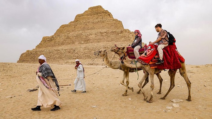 GIZA, EGYPT - MAY 4: Tourists ride on camels as Zoser Pyramid is seen behind at the historical Saqqara region, which is home to the majority of historical artifacts from ancient Egypt, in Giza, Egypt on May 4, 2025. King tombs, temples, small pyramids and the region, where the Zoser Pyramid, which is estimated to have been built in the 2700 B.C. is located, considered an open-air museum. (Photo by Nurettin Boydak/Anadolu via Getty Images)