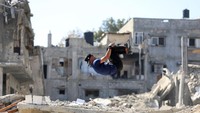 Anak muda melakukan aksi salto dalam olahraga Parkour di Jalur Gaza. Tampak di belakangnya reruntuhan bangunan yang hancur oleh rudal Israel.