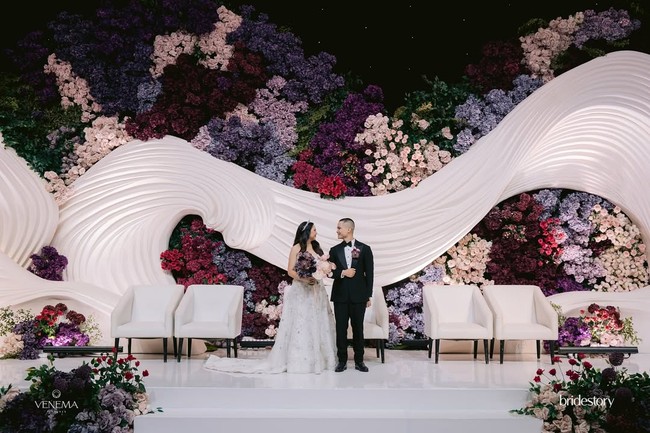 Pernikahan Cellos dan Natasha Putri terlihat mewah dengan dekorasi modern elegan ditambah sentuhan floral dramatis. Backdrop utama pelaminan Cellos menampilkan bentuk struktur putih bergelombang yang memberikan kesan dinamis dan mewah.  Foto: Dok. Instagram by.hilda