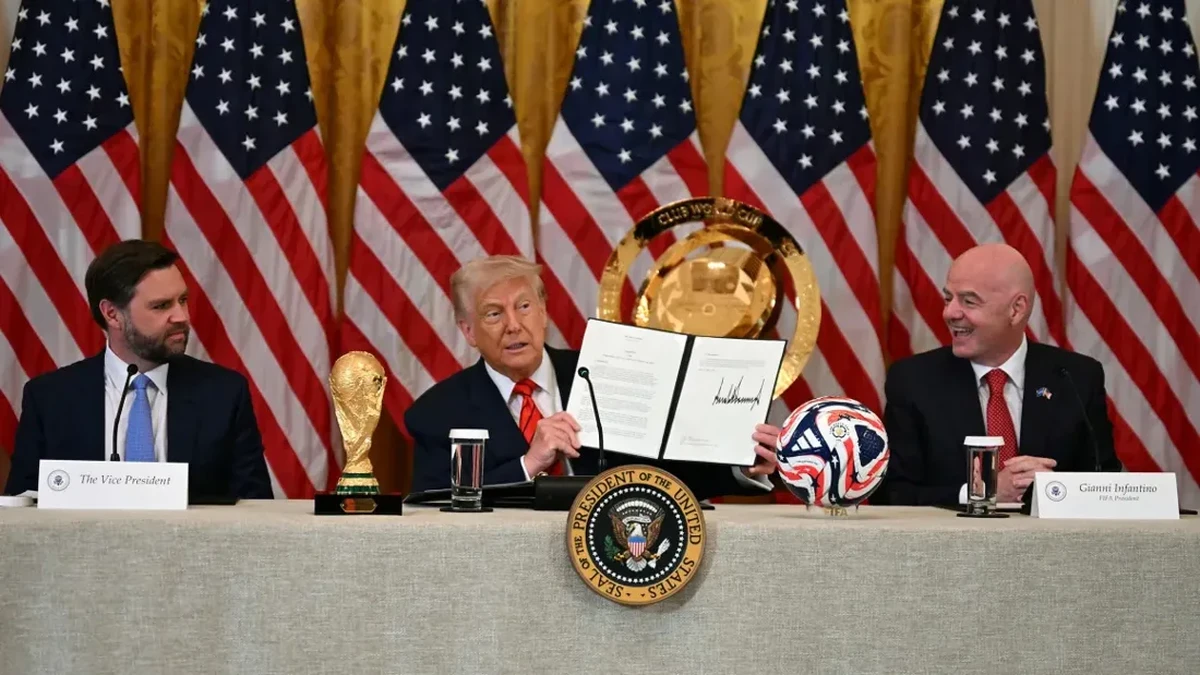 Presiden Donald Trump mengangkat dokumen yang membentuk Gugus Tugas Gedung Putih untuk Piala Dunia FIFA 2026 disaksikan oleh Wakil Presiden JD Vance dan Presiden FIFA Gianni Infantino (Jim Watson/AFP/Getty Images)