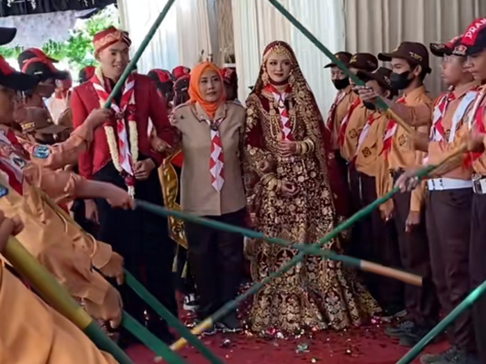 Pengantin ini mengenakan busana bernuansa India, tradisi adat Jawa dan juga menjalani prosesi tongkat pora Pramuka. Acara pernikahan tersebut langsung viral di TikTok.