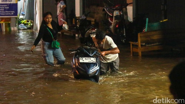 Warga mendorong motor menerobos banjir di Jalan Stadion, Wedomartani, Ngemplak, Sleman, Jumat (16/5/2025).