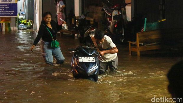 Warga mendorong motor menerobos banjir di Jalan Stadion, Wedomartani, Ngemplak, Sleman, Jumat (16/5/2025).