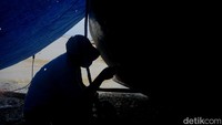 Seorang nelayan berteduh dibawah terpal saat memperbaiki perahu mereka yang mulai rusak.