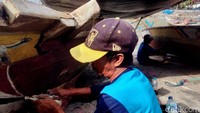 Para nelayan memilih memperbaiki perahu mereka saat berhenti melaut saat cuaca buruk.