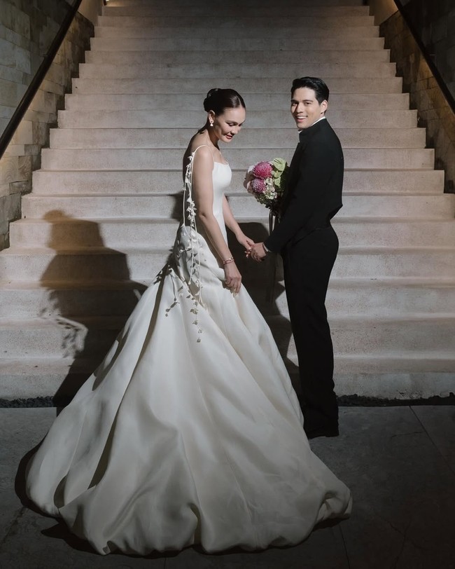 Resepsi malam hari, Luna Maya tetap setia dengan busana putih. Kali ini pilihan jatuh pada gaun sleeveless simple bernuansa ethereal rancangan Hian Tjen. Aksen bunga putih di bagian tali yang ditata menjuntai ke bawah memberi nuansa ethereal yang memukau. Foto: Instagram/@lunamaya @iluminen