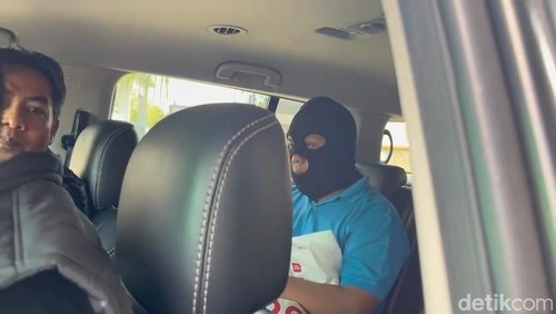 Dosen UIN Mataram berinisial WJ (mengenakan topeng) berada di dalam mobil penyidik seusai olah TKP kasus dugaan kekerasan seksual terhadap sejumlah mahasiswi, Kamis (22/5/2025). (Foto : Abdurrasyid Efendi/detikBali)