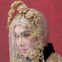 Penutup kepala didesain dengan veil transparan berhias aplikasi bordir bunga emas dan untaian mutiara kecil. Hiasan menyerupai mahkota floral berkilau yang dibentuk dengan teknik metalwork, menghadirkan nuansa fantasi dan regalia. Foto: Instagram/@princessyahrini @aldiphoto