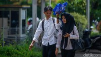 Di tengah terik, seorang wanita pulang dari Job Fair sambil dipayungi tas biru oleh rekan prianya—potret kebersamaan usai harapan dicari.