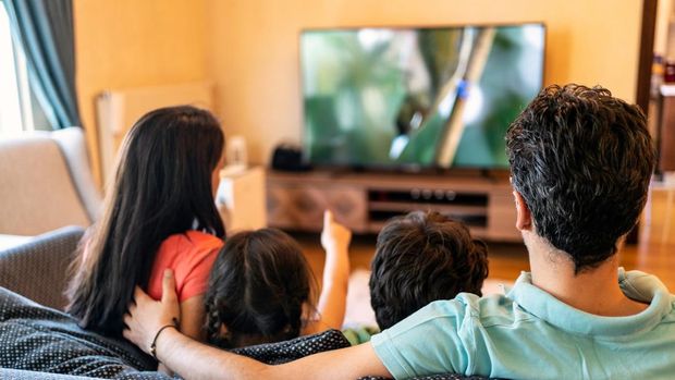 Ilustrasi menonton televisi bersama keluarga Parents and their two children watching TV together at home