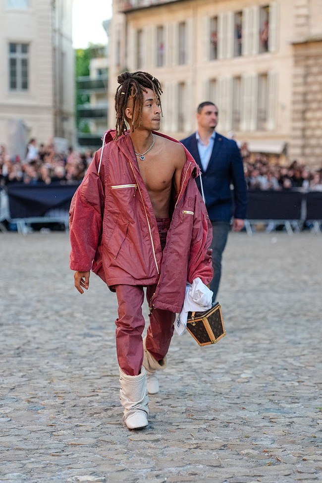 Aktor dan musisi 25 tahun ini memilih setelan monokrom marun berupa jaket parka bergaya windbreaker oversized dengan detail hardware mencolok. Volume besar, kantong dada beresleting, serta hem mengerut membuat tampilannya terkesan seperti jas hujan mewah. Parka dipadukan dengan celana dan hoodie senada. Foto: Getty Images/Edward Berthelot