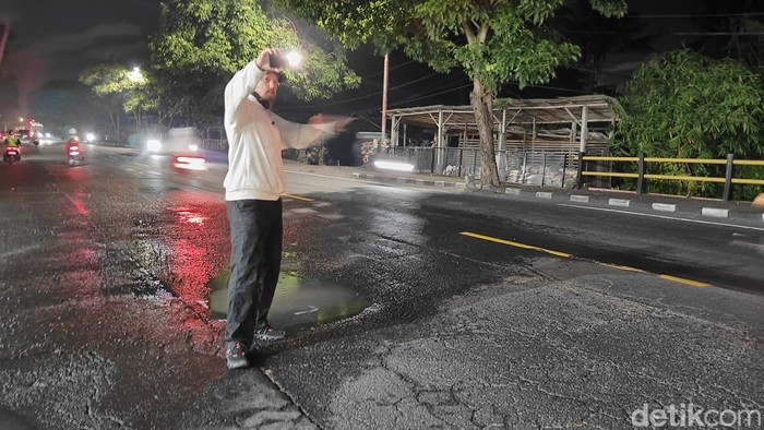 Seorang WNA membantu mengatur lalu lintas dan memperingatkan pengendara berhati-hati ada jalan berlubang di Jalan Denpasar-Gilimanuk, Kelurahan Kapal, Badung, Bali, Senin (26/5/2025). (FotoAgus Eka/detikBali)