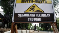 Petugas memasang papan peringatan proyek perbaikan trotoar.   