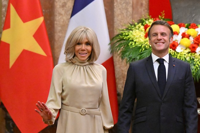Macron tampak mengenakan setelan jas navy, sementara Brigitte tampil elegan berbalut kerah tinggi bernuansa beige. Ikat pinggang berwarna senada hadir mengaksentuasi siluet rampingnya. Foto: via REUTERS/NHAC NGUYEN