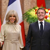 Macron tampak mengenakan setelan jas navy, sementara Brigitte tampil elegan berbalut kerah tinggi bernuansa beige. Ikat pinggang berwarna senada hadir mengaksentuasi siluet rampingnya. Foto: via REUTERS/NHAC NGUYEN