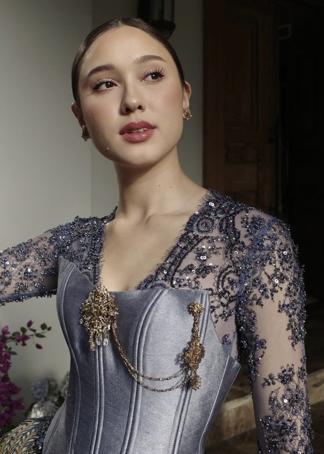 Atasan kebaya berbentuk korset berwarna lilac keperakan itu dilapisi dengan brokat berpayet halus dan memperlihatkan detail bordir floral dramatis di sepanjang lengan panjang transparan. Potongan sweetheart neckline yang berpadu dengan detail V-neck dalam aksen renda menghadirkan kesan feminin yang tetap berwibawa. Foto: dok. Instagram @yasminnapper