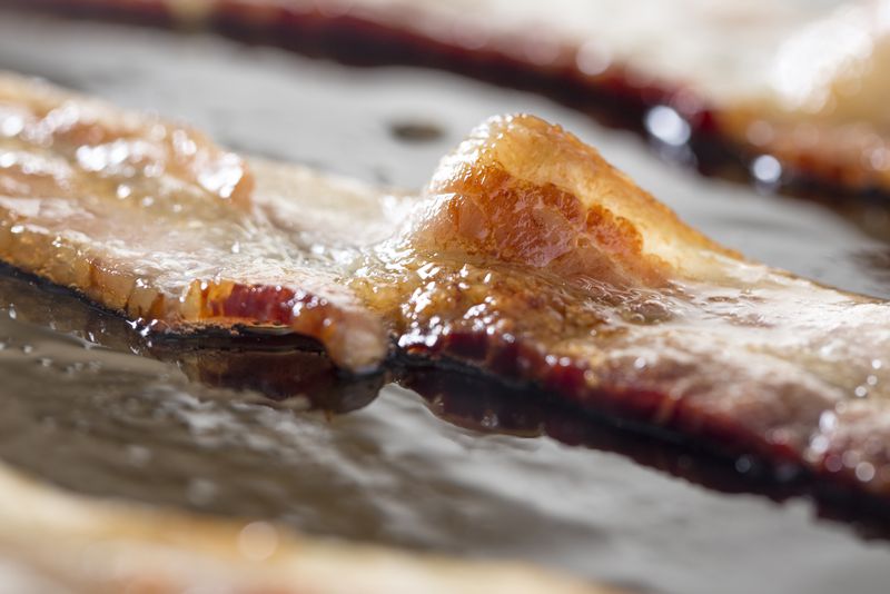 Macro of strips of bacon cooking in a frying pan.