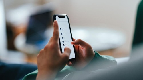 Unrecognizable teenage boy typing text messages on his smartphone while lying on a couch at home.