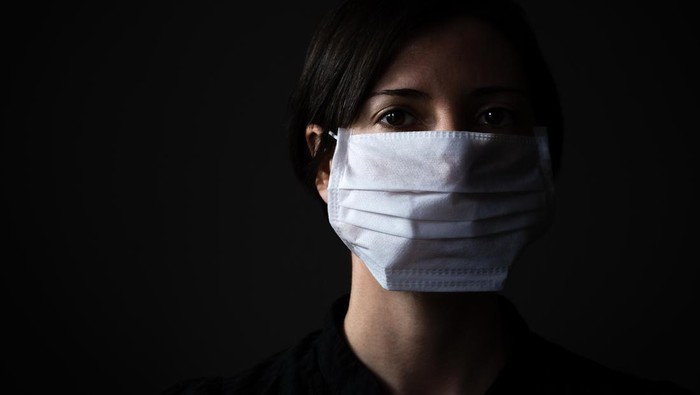 Adult woman wearing hygienic mask to prevent infection, airborne respiratory illness such as flu, 2019-nCoV on dark background. Healthcare concept.