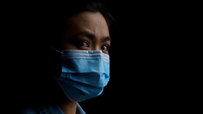 Asian woman wearing protective mask isolated on background. Low key.