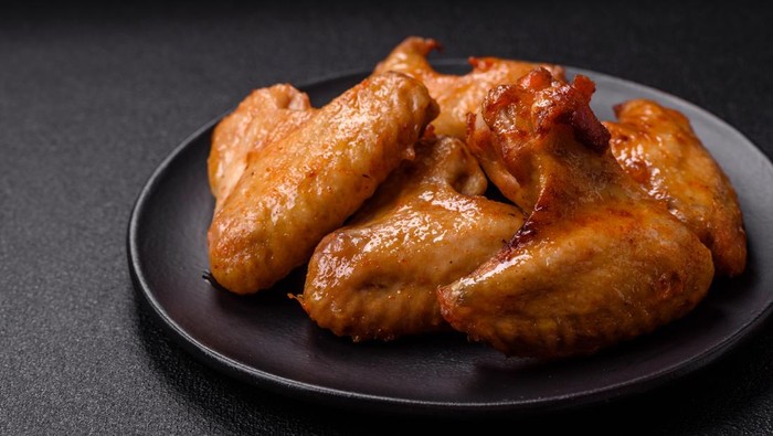 Delicious fried chicken wings with salt, spices and herbs on a dark concrete background