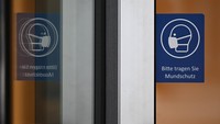 Stiker pengingat untuk pakai masker di pintu masuk sebuah gedung di Frankfurt. Foto: Getty Images/Spencer Platt