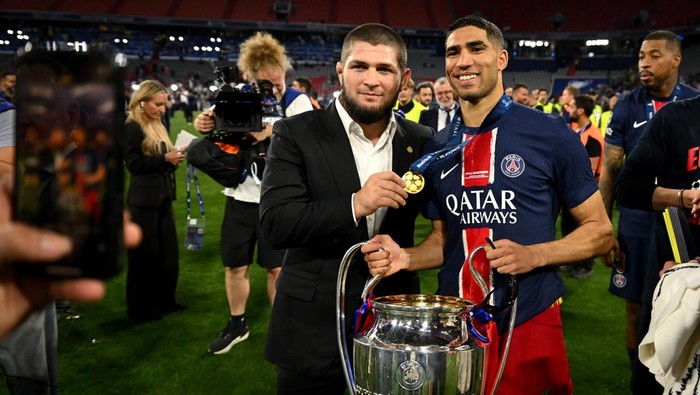 MUNICH, GERMANY - MAY 31: Achraf Hakimi of Paris Saint-Germain poses for a photograph with the UEFA Champions League trophy alongside former mixed martial artist Khabib Nurmagomedov after his teams victory, to secure Paris Saint-Germains first ever UEFA Champions League title in the clubs history and a record UEFA Champions League Final winning scoreline of 5-0, following the UEFA Champions League Final 2025 between Paris Saint-Germain and FC Internazionale Milano at Munich Football Arena on May 31, 2025 in Munich, Germany. (Photo by Michael Regan - UEFA/UEFA via Getty Images)