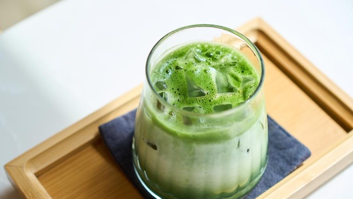 Vibrant green iced matcha latte is being prepared on a wooden tray
