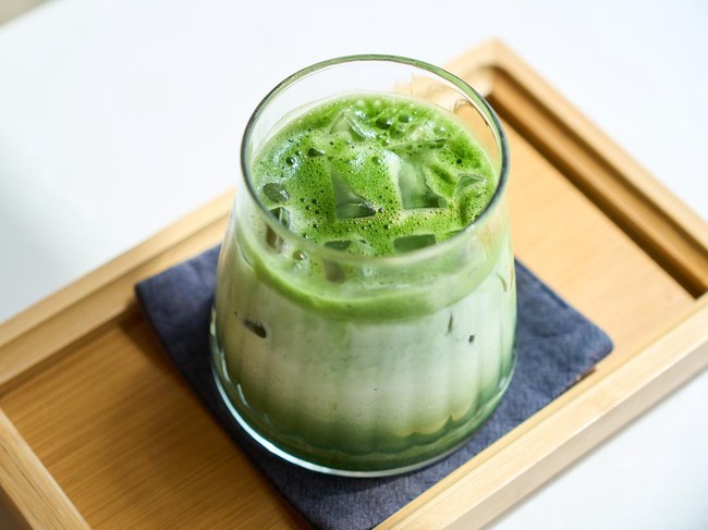 Vibrant green iced matcha latte is being prepared on a wooden tray