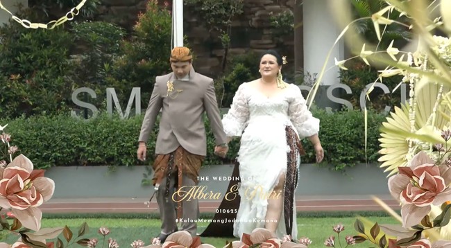 Keduanya juga sempat berganti pakaian namun tetap dengan menerapkan unsur tradisional. Rafli mengenakan beskap coklat muda dipadukan dengan kain jarik Jawa. Sementara Putri mengenakan gaun putih berbelahan hingga ke paha. Gaun tersebut memiliki tambahan aksen kain batik coklat untuk mempertahankan unsur tradisionalnya. Foto: YouTube/Putri Habibie