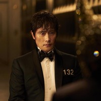 Front Man (pemain Lee Byung Hun) berhasil mengelabui Seong Gi Hun setelah menyusup sebagai peserta permainan bertahan hidup. Tampil memakai setelan jas hitam. Dalam trailer drama Korea Squid Game 3, dia menanyakan apakah Seong Gi Hun masih percaya dengan manusia. Foto: dok. Netflix