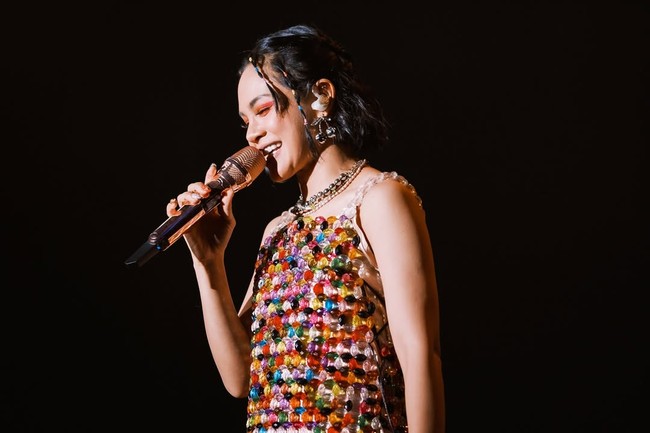 Potongannya mengingatkan pada estetika 1960-an, tapi permainan warna dan cahaya dari materialnya membuat tampilan Andien tetap terasa kekinian. Ia memadukan gaun itu dengan sepatu boots putih setinggi lutut, ikon mutlak gaya go-go dancer, sekaligus simbol kebebasan perempuan di era itu. (Foto: Instagram/@andien)