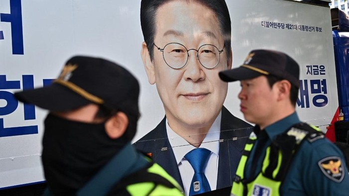 Police officers stand next to placard of South Korean presidential candidate Lee Jae-myung of the Democratic Party outside the MBC media centre ahead of a televised presidential debate for the forthcoming June 3 presidential election in Seoul on May 27, 2025. (Photo by Pedro Pardo / AFP)