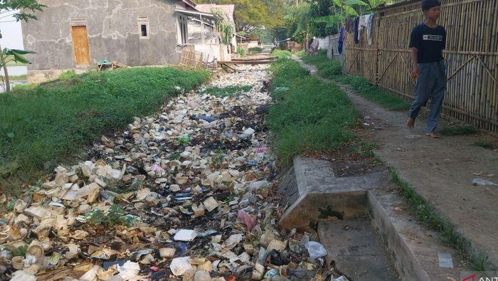 Seorang warga sedang melintas didekat saluran irigasi yang dipenuhi sampah di Kampung Sumur Bor, Desa Sampang, Kecamatan Tirtayasa, Kabupaten Serang, Banten, Senin (2/6/2025).