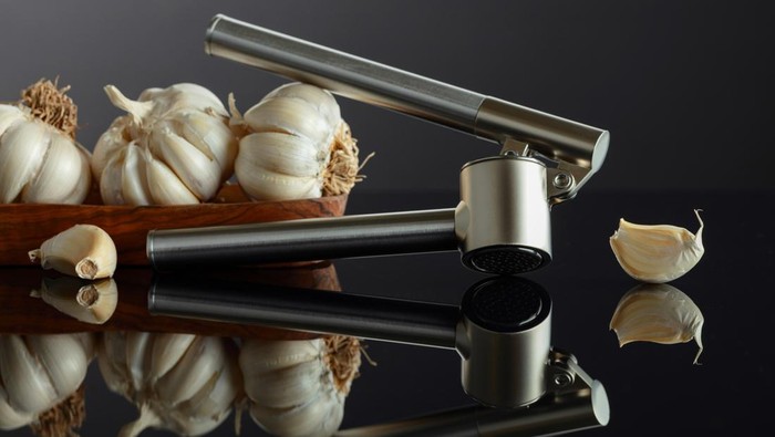 Garlic bulbs and garlic press on a black reflective background.