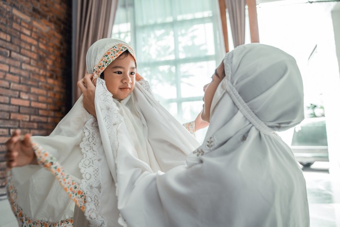 muslim mother help her young daughter to put the scarf on before pray